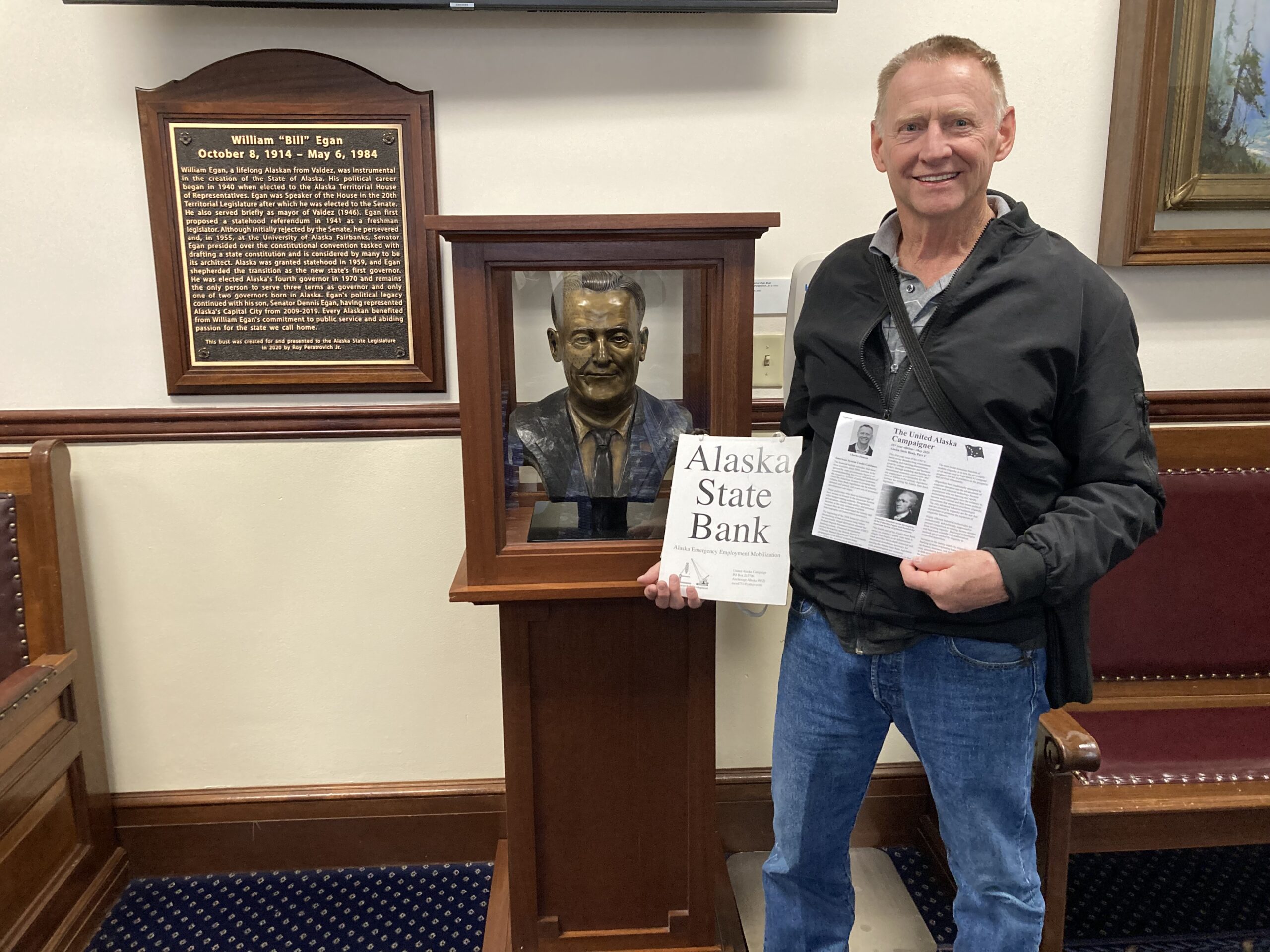 Charles Duncan passing out Part 4 of the Alaska State Bank series in the state capital in front of a bust of Bill Egan who was one of the founders of the State of Alaska.